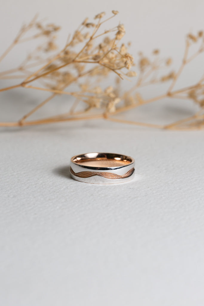 Mens white and rose gold wedding ring with a pattern going all the way around it