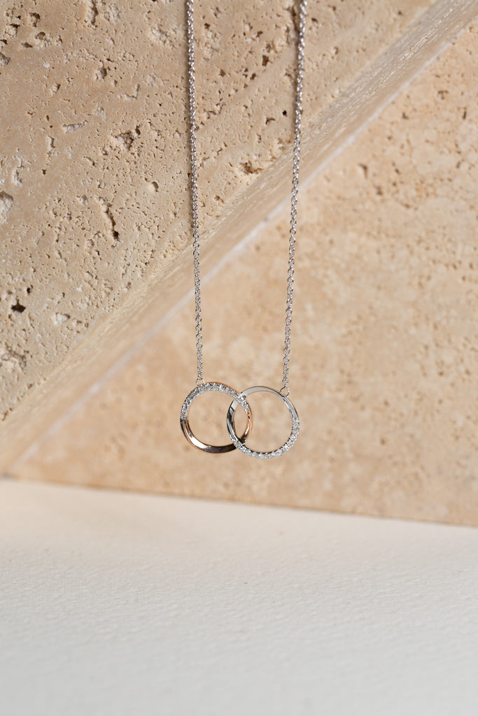 white gold and rose gold double circle necklace with diamonds on it