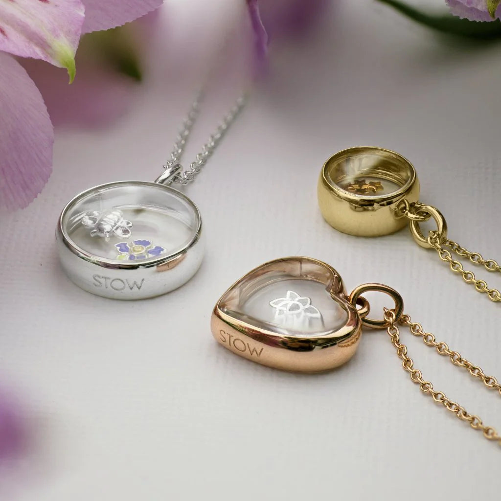 Three Stow Lockets with charms inside them.  One is silver, one is gold, and one is rose gold.