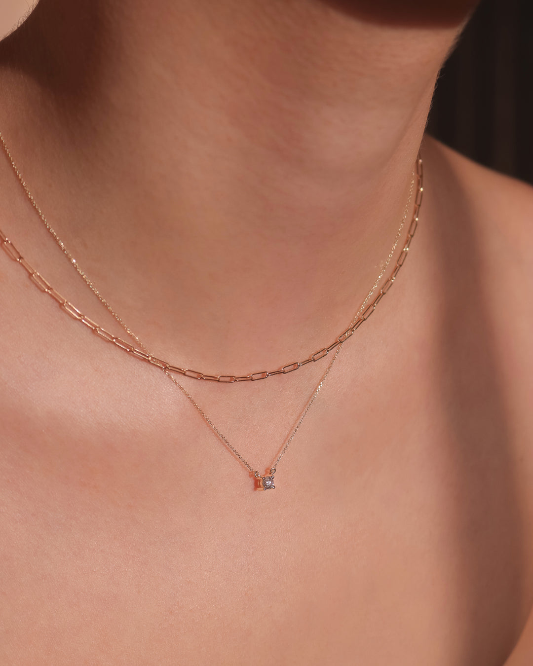 A fine paperclip necklace is worn layered with a diamond solitaire necklace.