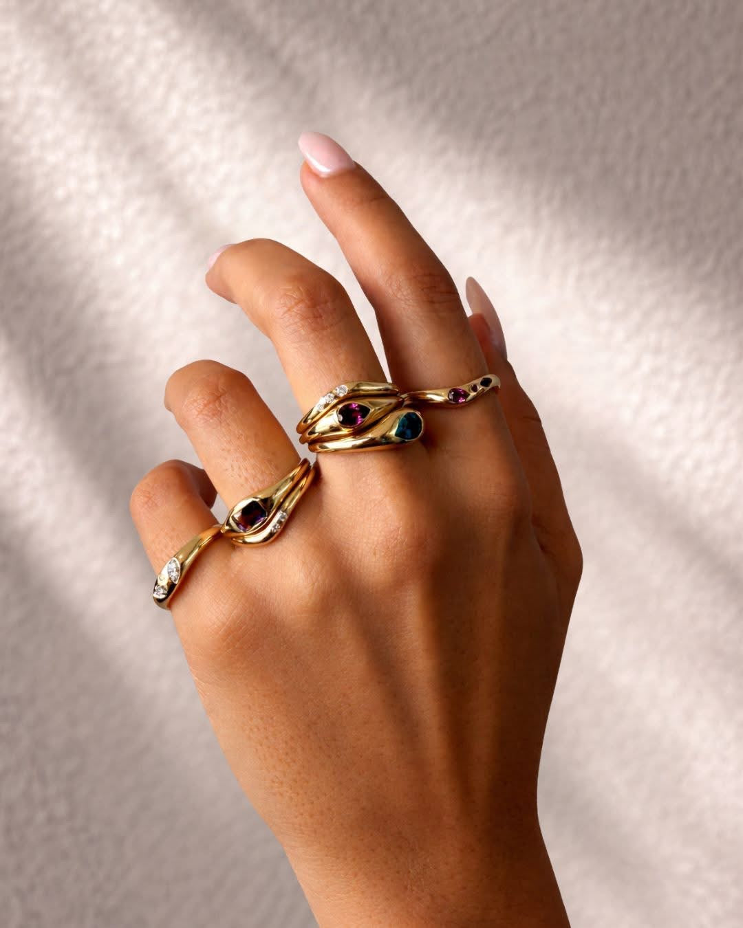 A womens hand wearing stacks of gold rings, which are set with diamonds and coloured gemstones.