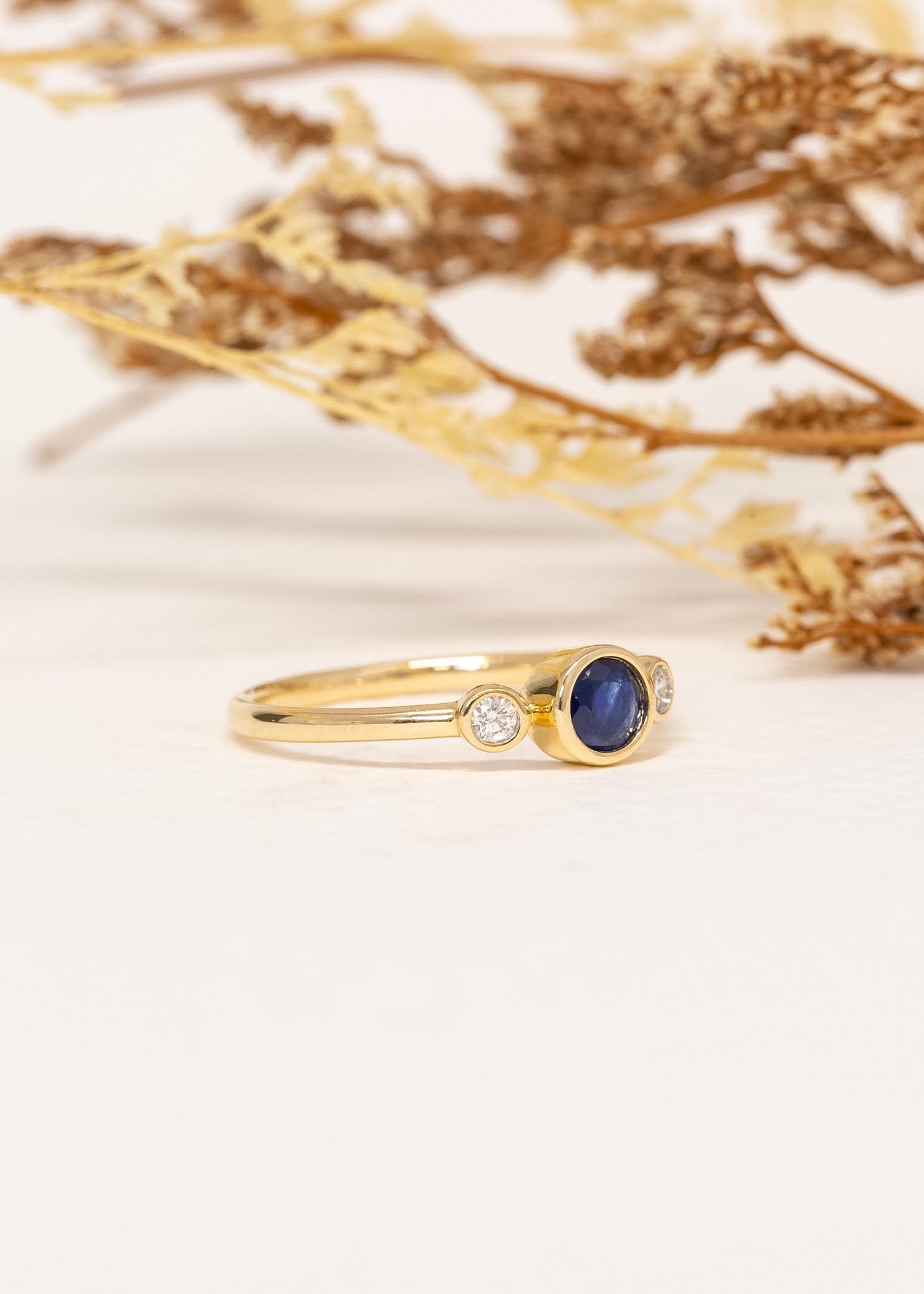 Aria Sapphire Ring in 9ct yellow gold with natural blue sapphire and diamonds, styled with dried foliage