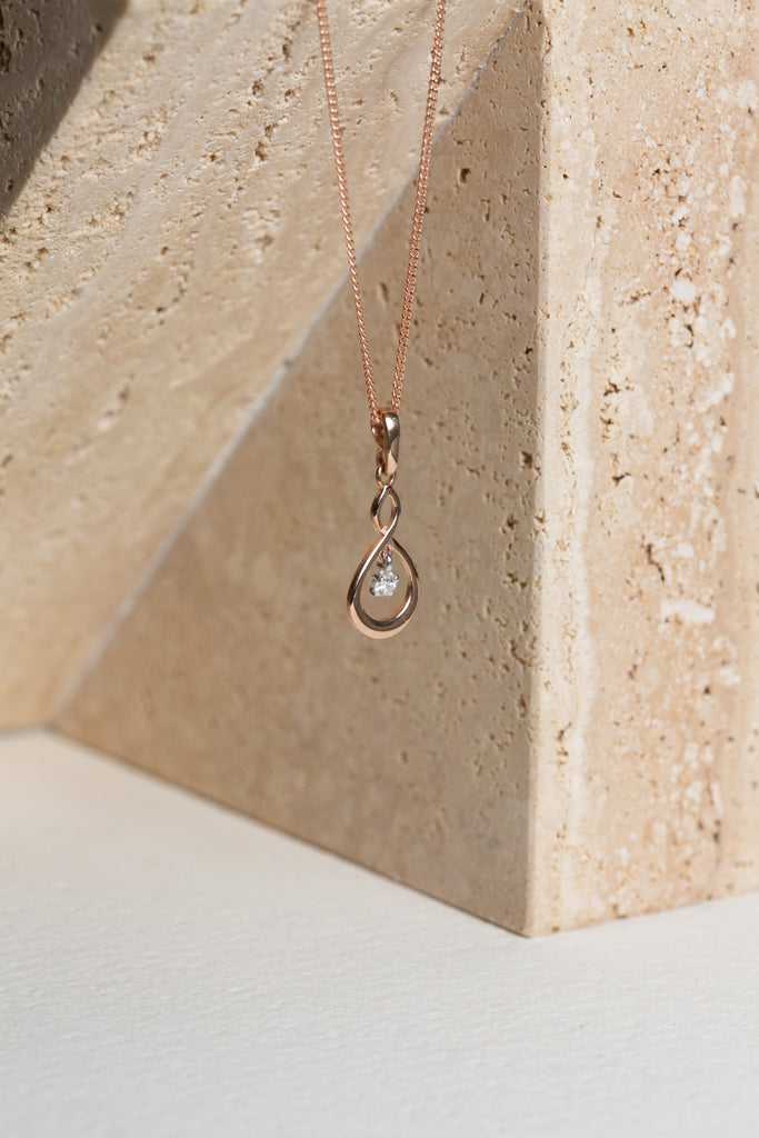 rose gold infinity twist necklace with a single diamond set in it
