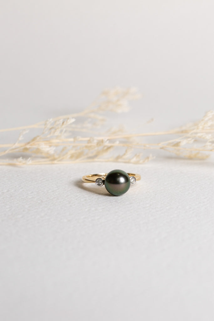 A large Tahitian Pearl is set on a gold band, with diamonds either side.