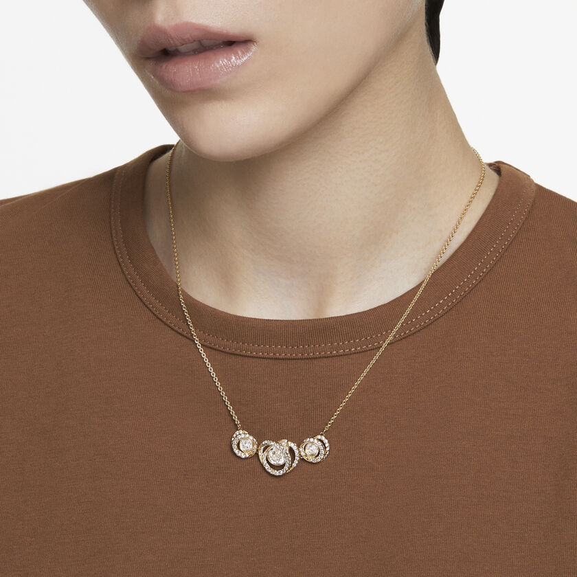 A model is wearing a gold Swarovski crystal necklace over the top of a brown t shirt