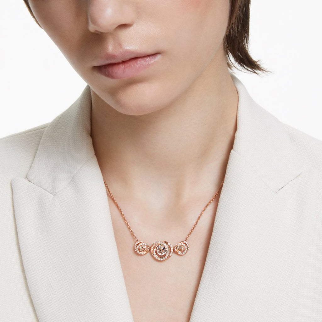 A model is wearing a rose gold Swarovski crystal necklace with a white blazer.