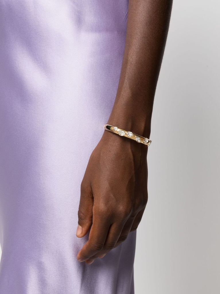 A model is wearing a gold Swarovski Dextera bangle.  She is wearing a purple silk dress.