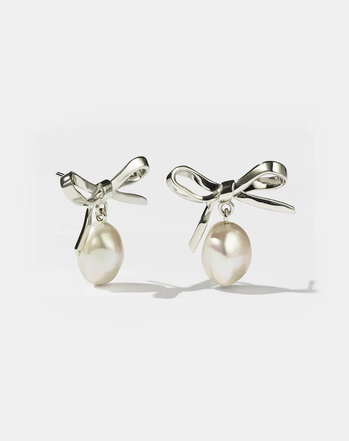 Silver bow earrings with pearls hanging from them