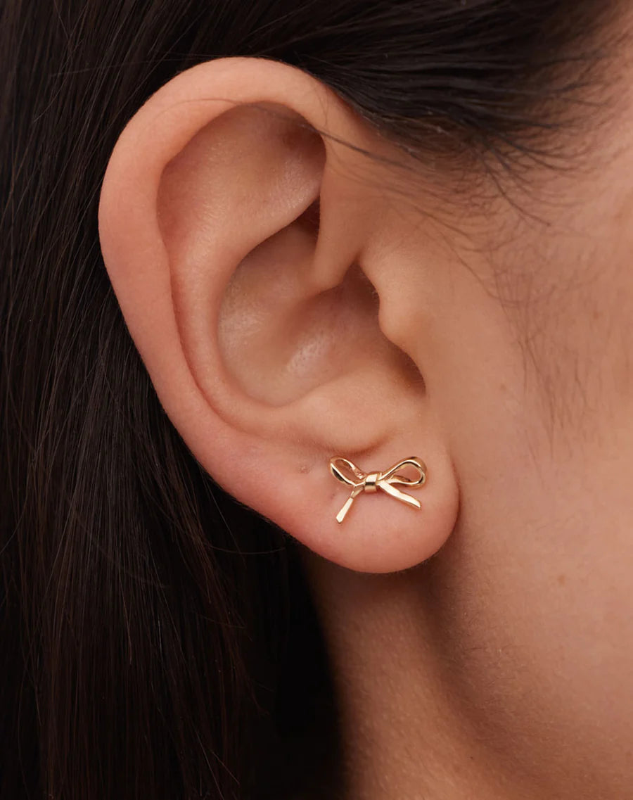 A model is wearing a pair of Meadowlark bow stud earrings
