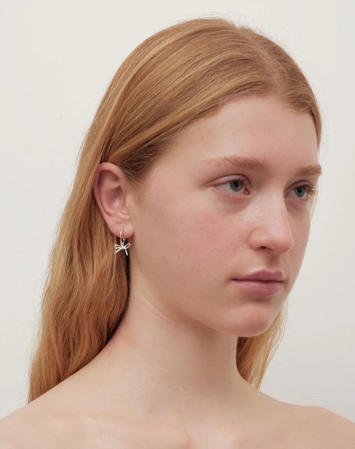 Model wearing silver hoop earrings with bows on them