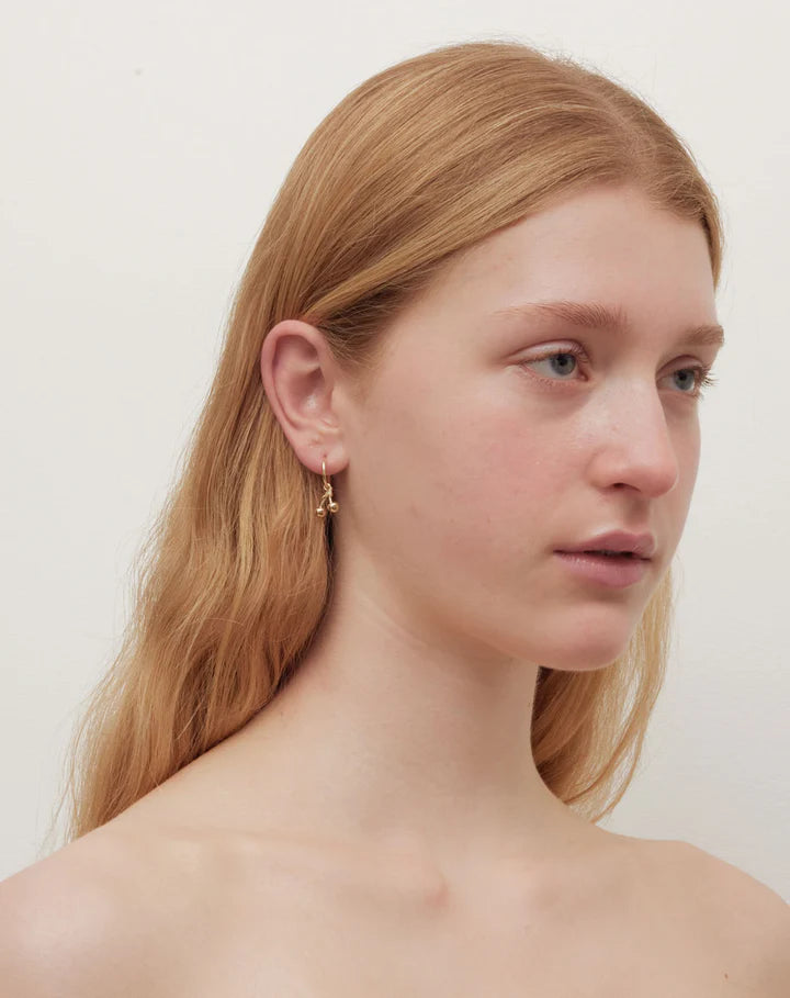 A redheaded model is wearing cherry hoop earrings.